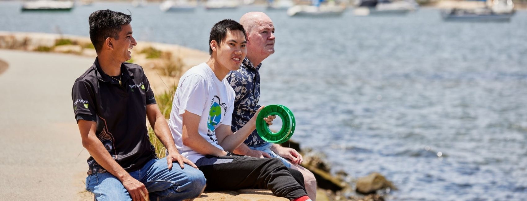 Two participants hanging out near the water with fishing line supported by an Ability Options staff member