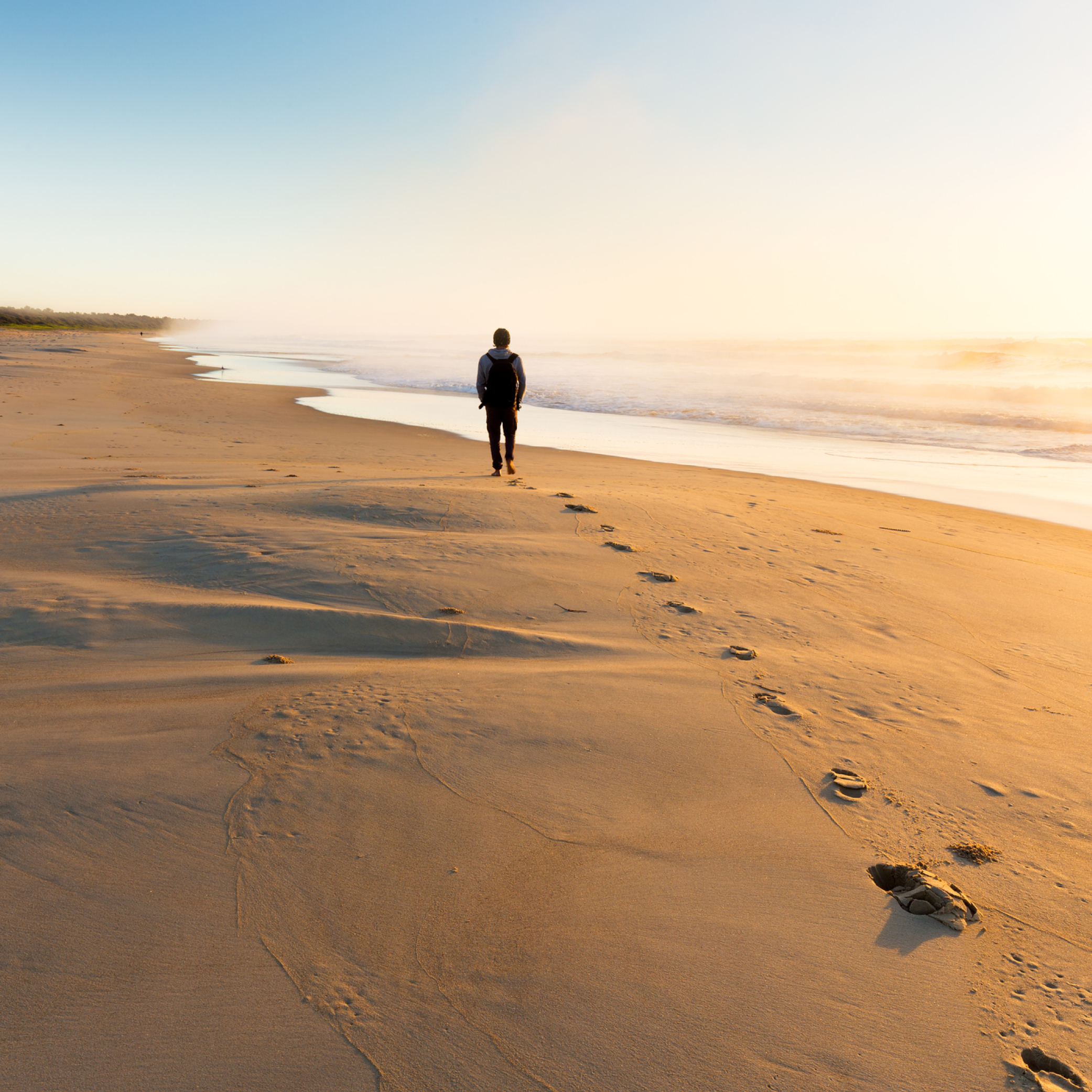 a man walking on the beach, leaving footsteps behind