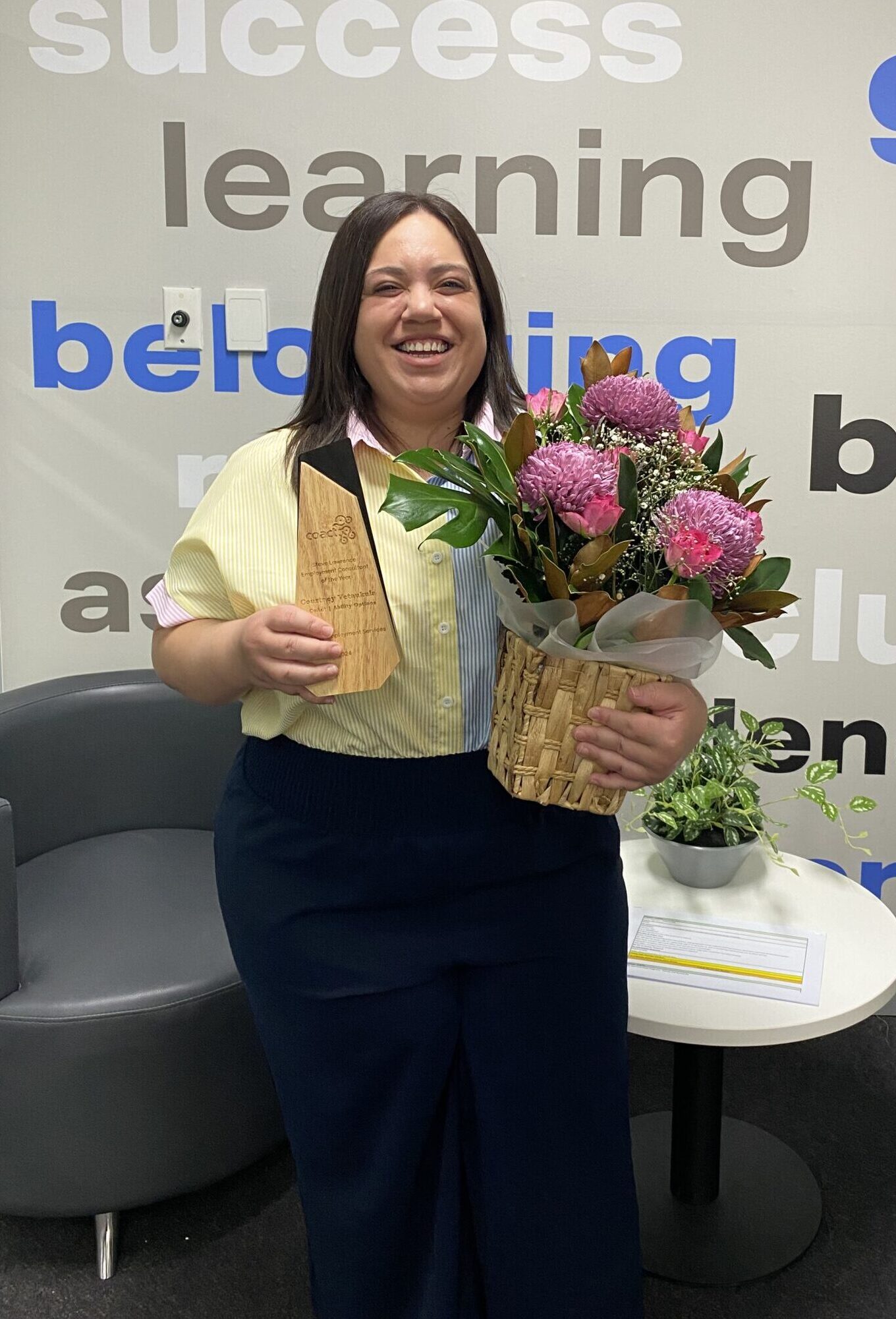 Ability Options’ Hornsby Workforce Partner Courtney smiling as she holds flowers and the top award from CoAct for her excellence in helping people find employment.