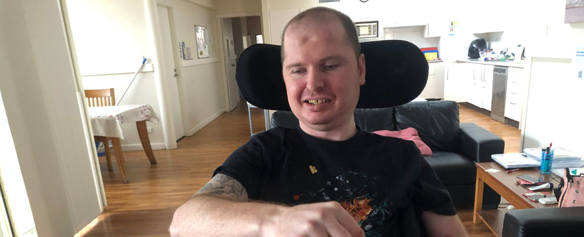 Photo of a man using an electric wheelchair, sitting at a table smiling